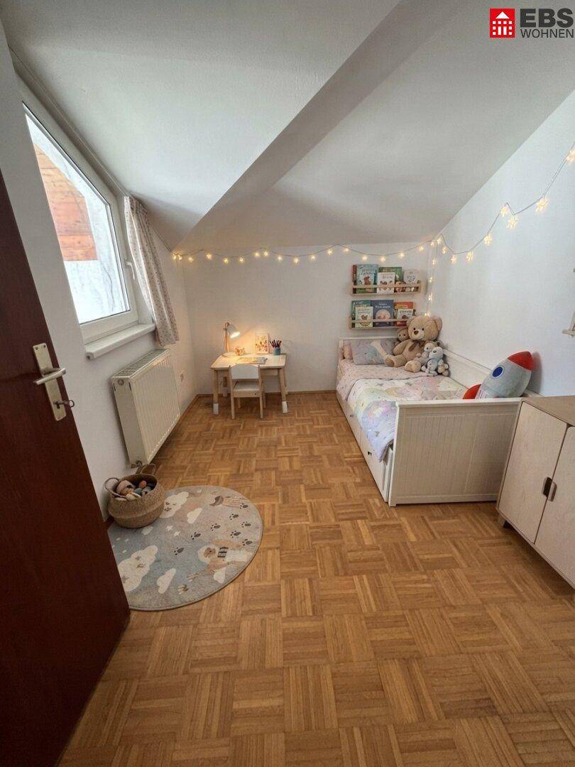 Gemütliches Kinderzimmer mit Parkettboden, Schreibtisch, Fenster und verspielter Dekoration.