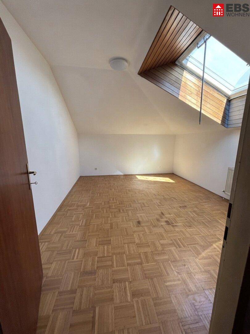 Leeres Zimmer im Dachgeschoss mit Parkettboden und großem Dachfenster, ideal für ein Schlafzimmer.