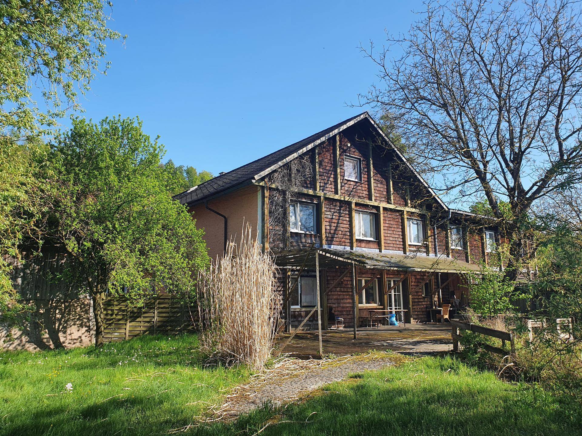Gebäude mit Holzfassade, großen Fenstern und überdachter Terrasse umgeben von Natur.