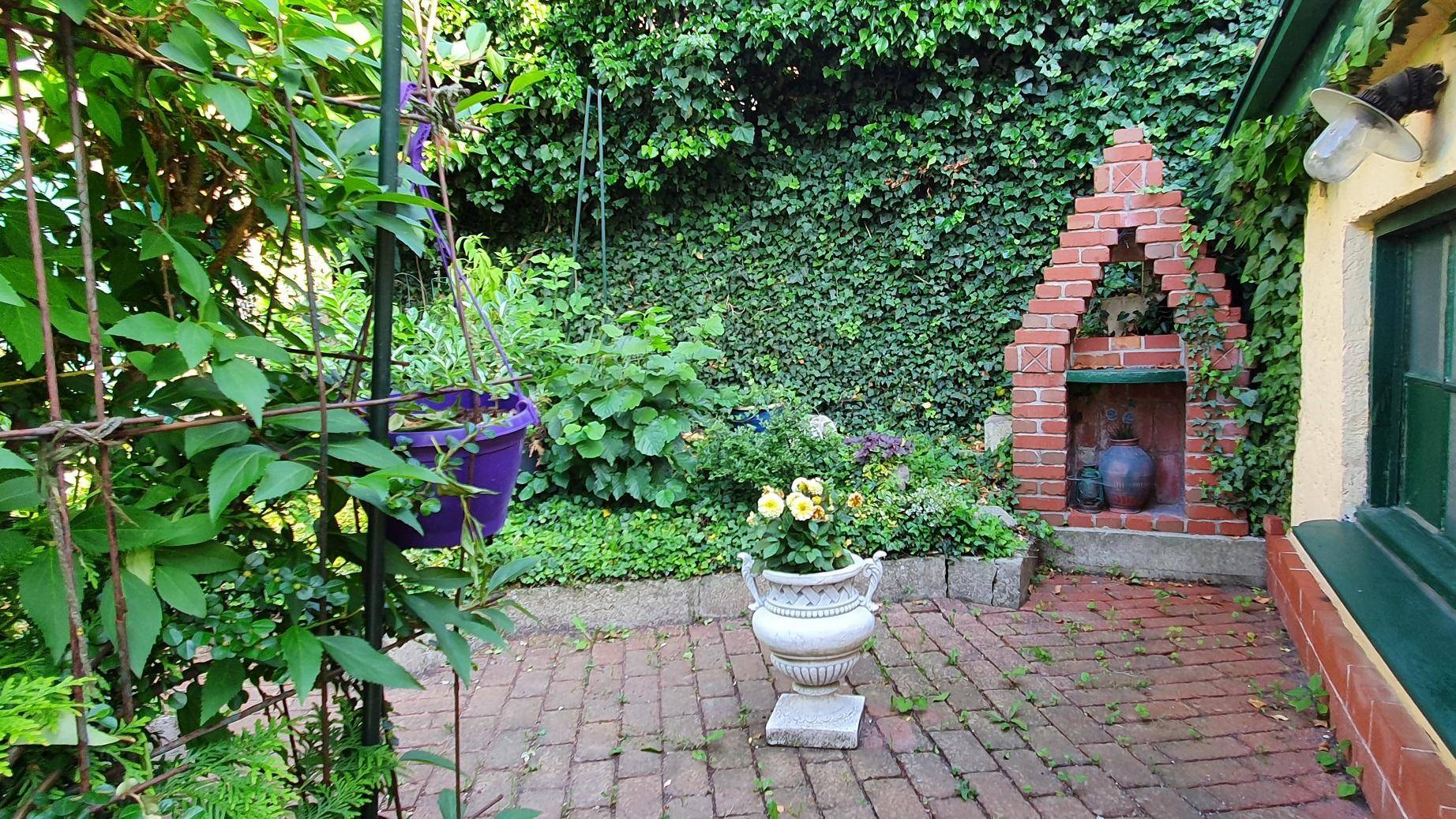 Kleiner Gartenbereich mit Ziegelpflaster, gemauertem Grill und üppigem Efeu an der Wand.