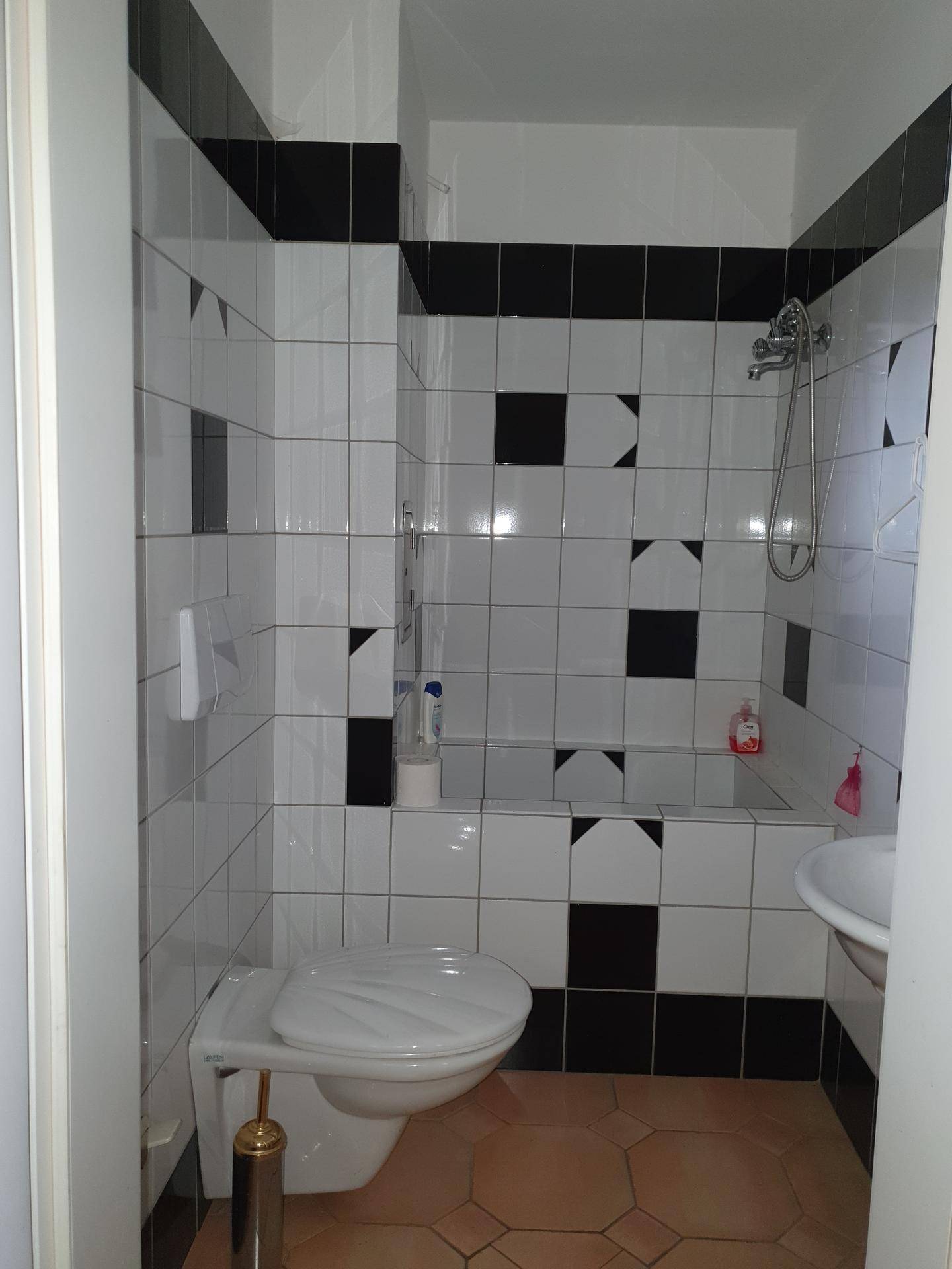 Kleines Badezimmer mit markanten schwarz-weißen Fliesen, Toilette und Dusch-Badewannen-Kombination.