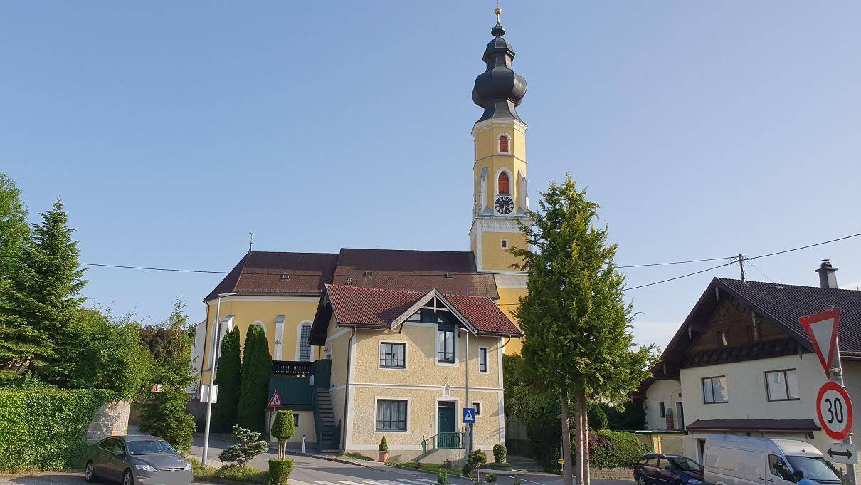Historisches Gebäude mit markantem Kirchturm im Hintergrund, umgeben von einer ruhigen Straße.
