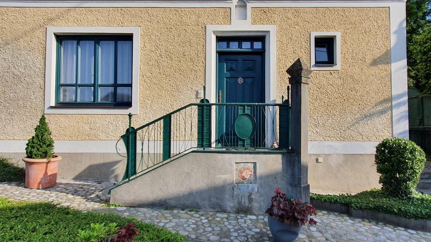 Eingangsbereich des Hauses mit grüner Tür, Treppe und gepflastertem Vorplatz, einladend gestaltet.