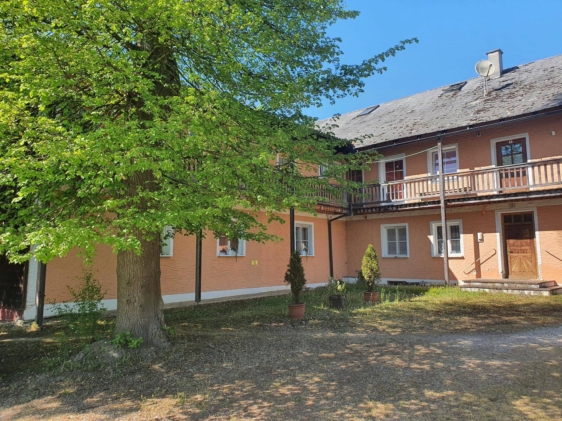 Traditionelles Gebäude mit ockerfarbener Fassade, Holzbalkonen und altem Baumbestand.
