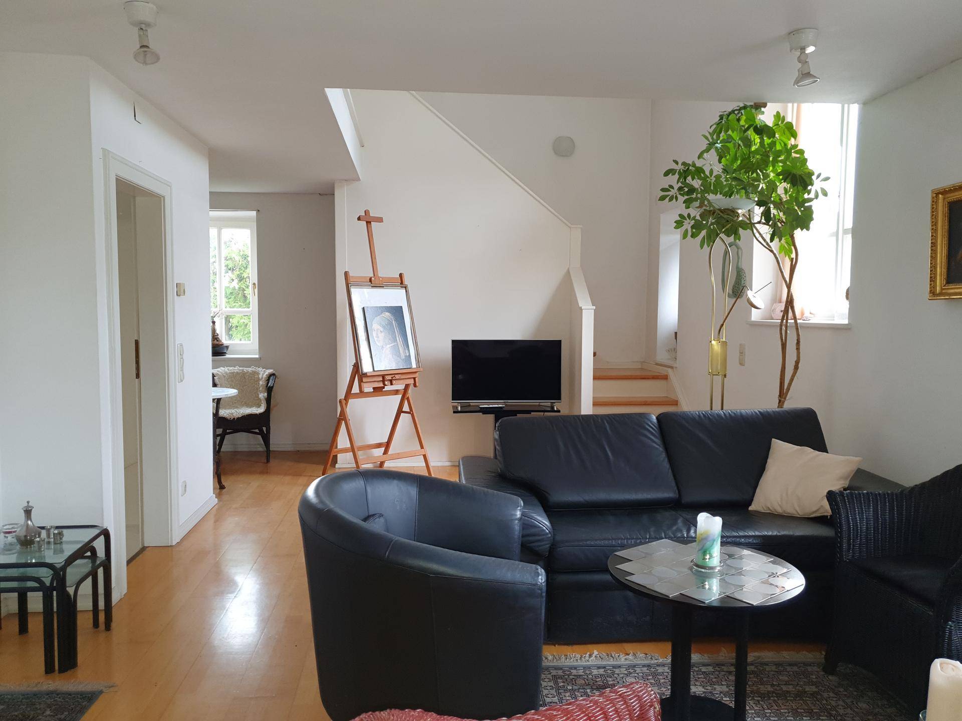 Wohnzimmer mit Treppenaufgang, bequemer Ledercouch und hellem Holzboden, offen gestaltet.