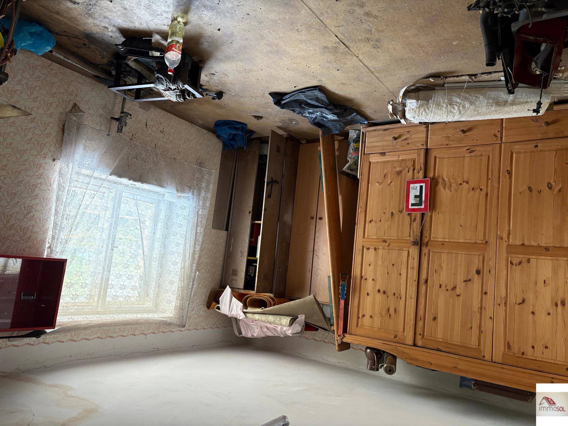 Unaufgeräumter Innenraum mit einem großen Holzschrank und einem Fenster, das Licht in den Raum bringt.