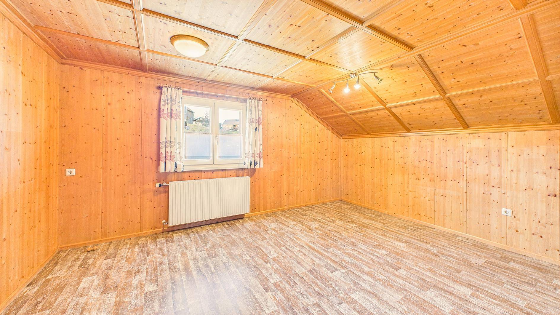 Helles Zimmer mit Holztäfelung, Dachschräge und Fenster, bereit zur individuellen Gestaltung.
