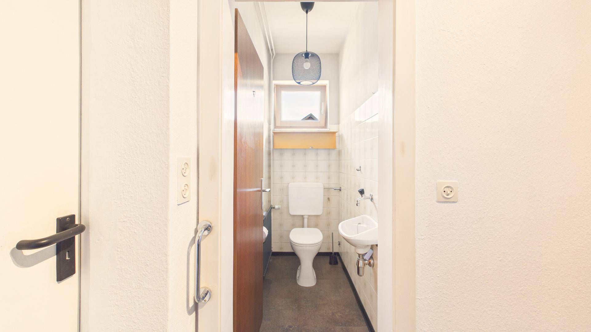 Kleines Gäste-WC mit Fenster, Toilette und Waschbecken, hell gefliest.