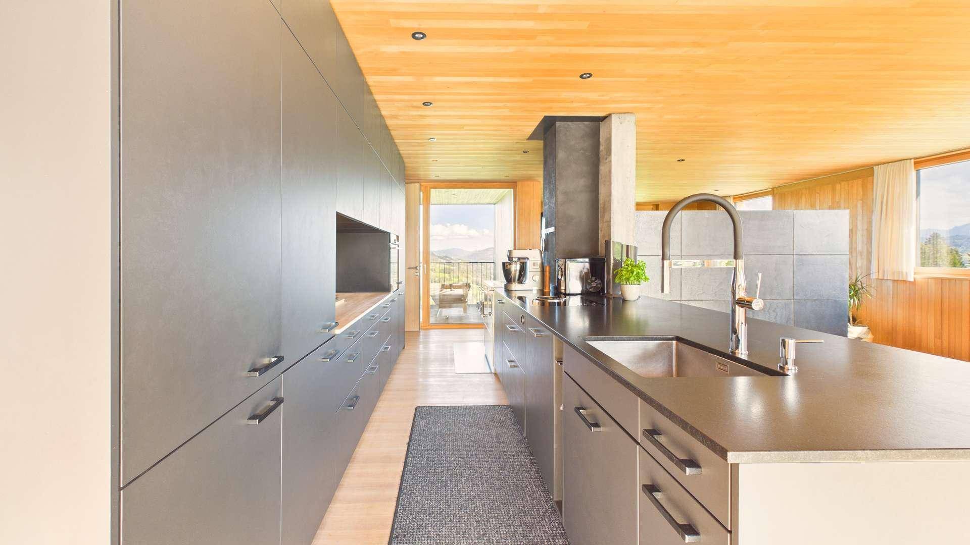 Moderne Küche mit dunklen Schränken, integrierten Geräten und Arbeitsplatte, offen zum Wohnbereich.