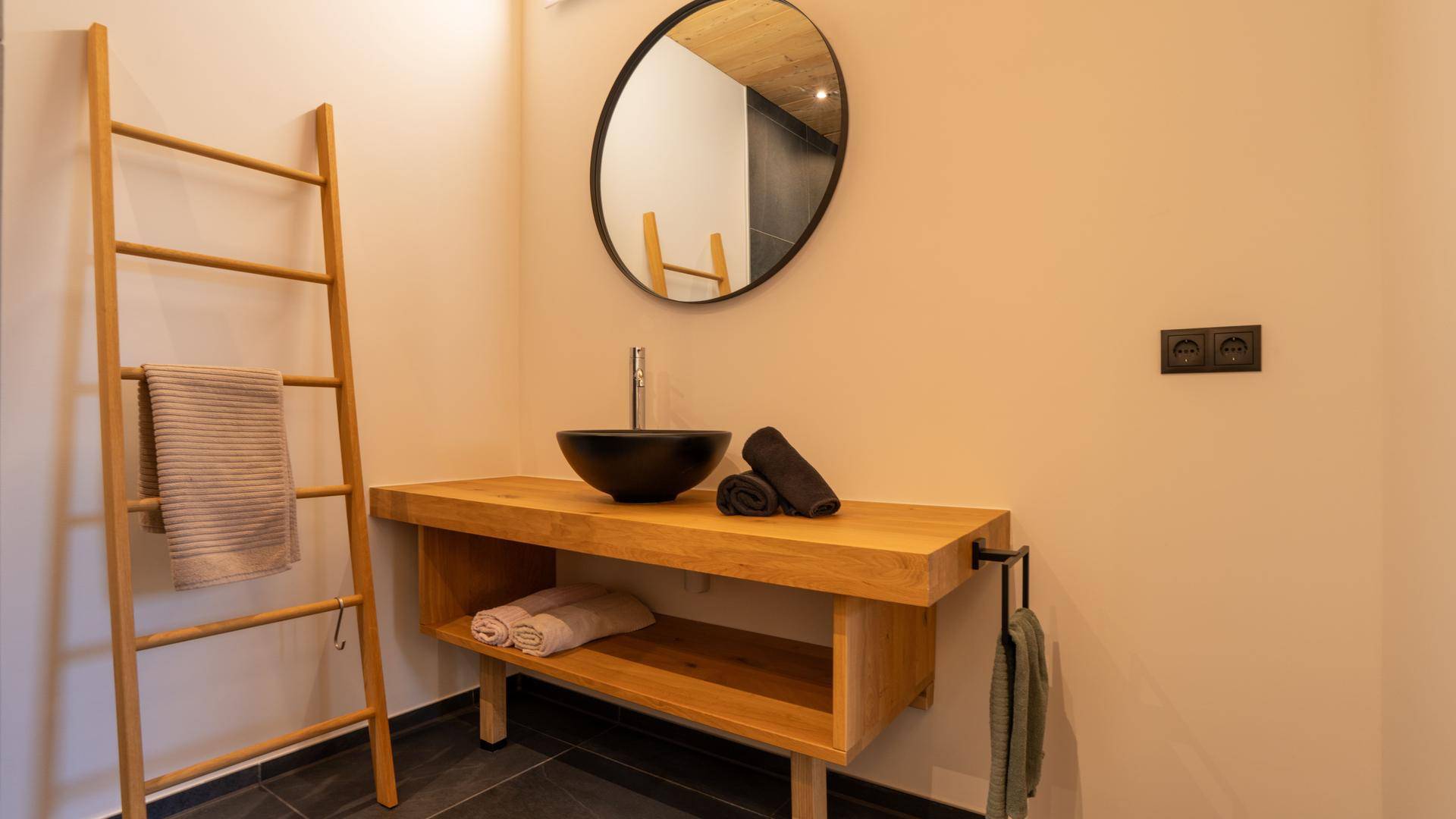 Badezimmer mit modernem Holzwaschtisch, Aufsatzwaschbecken und rundem Spiegel.
