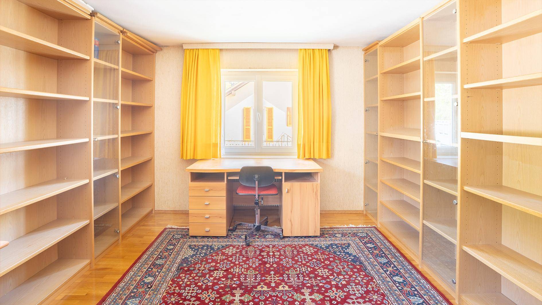 Arbeitszimmer mit vielen Bücherregalen, Schreibtisch und einem Teppich.