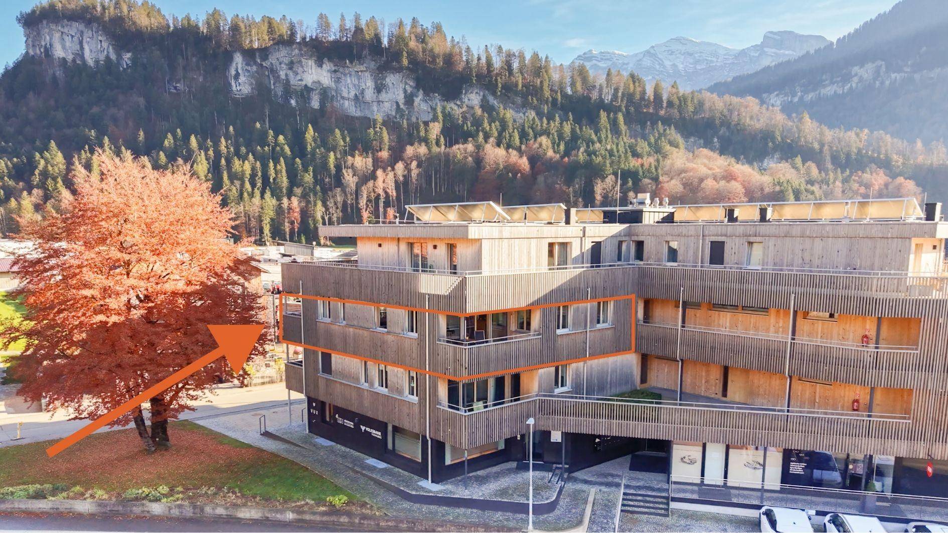 Modernes Mehrfamilienhaus mit Holzfassade, Balkonen und Bergblick.