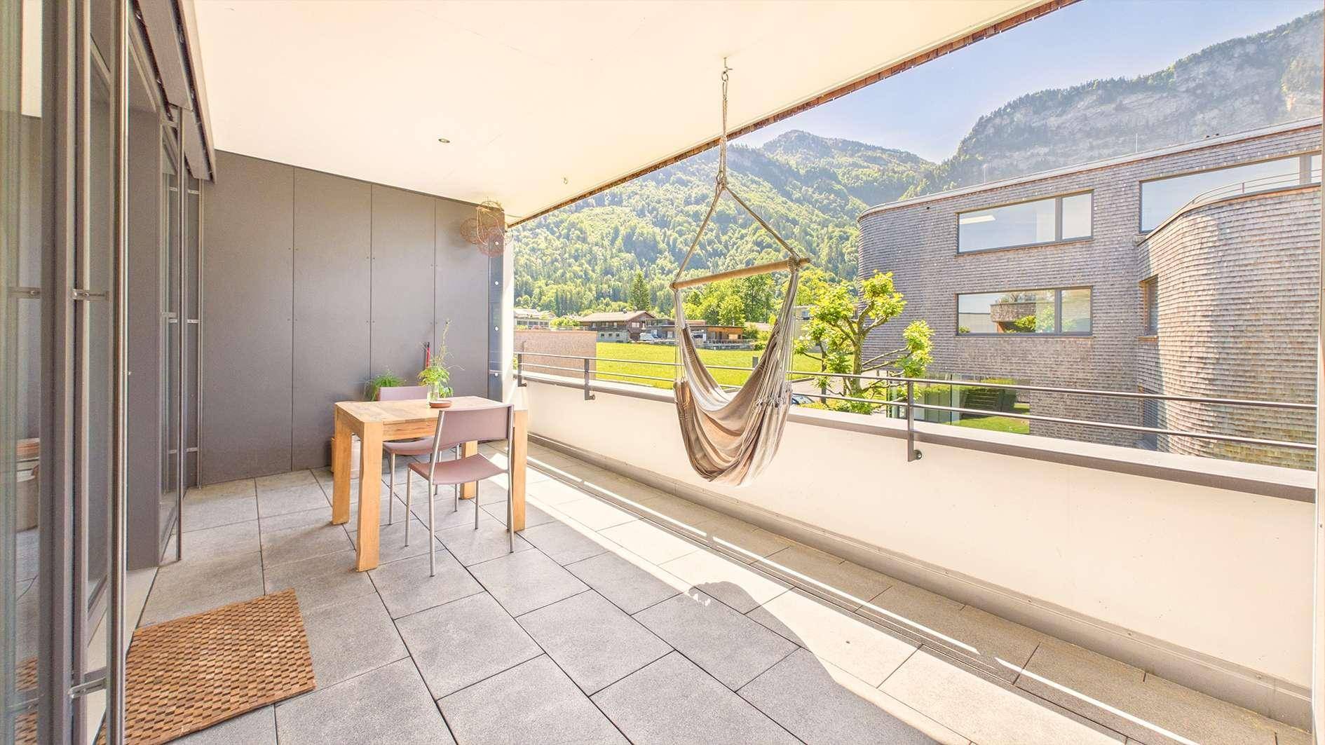 Sonniger Balkon mit Bergblick, Sitzgelegenheiten und Hängematte.