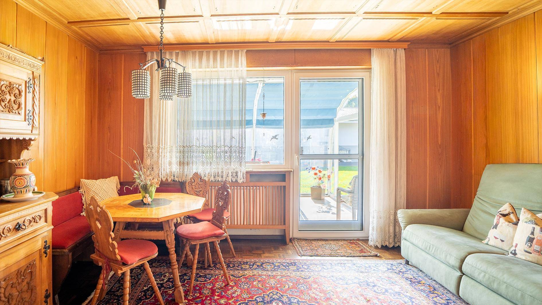 Rustikaler Wohn-Essbereich mit Holzvertäfelung, traditionellen Möbeln und Teppich.