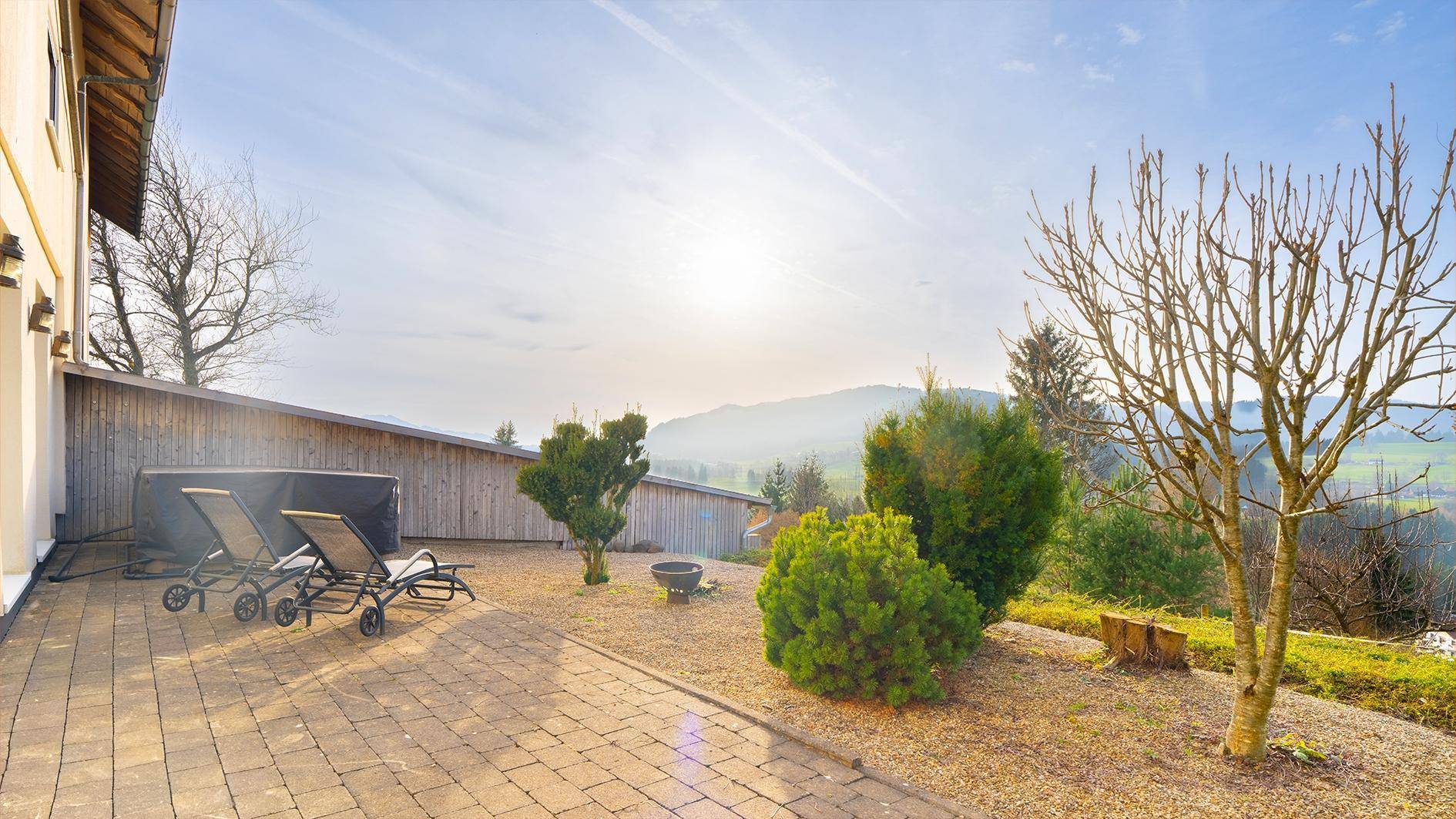 Große gepflasterte Terrasse mit Liegestühlen und weitem Blick über die hügelige Landschaft.