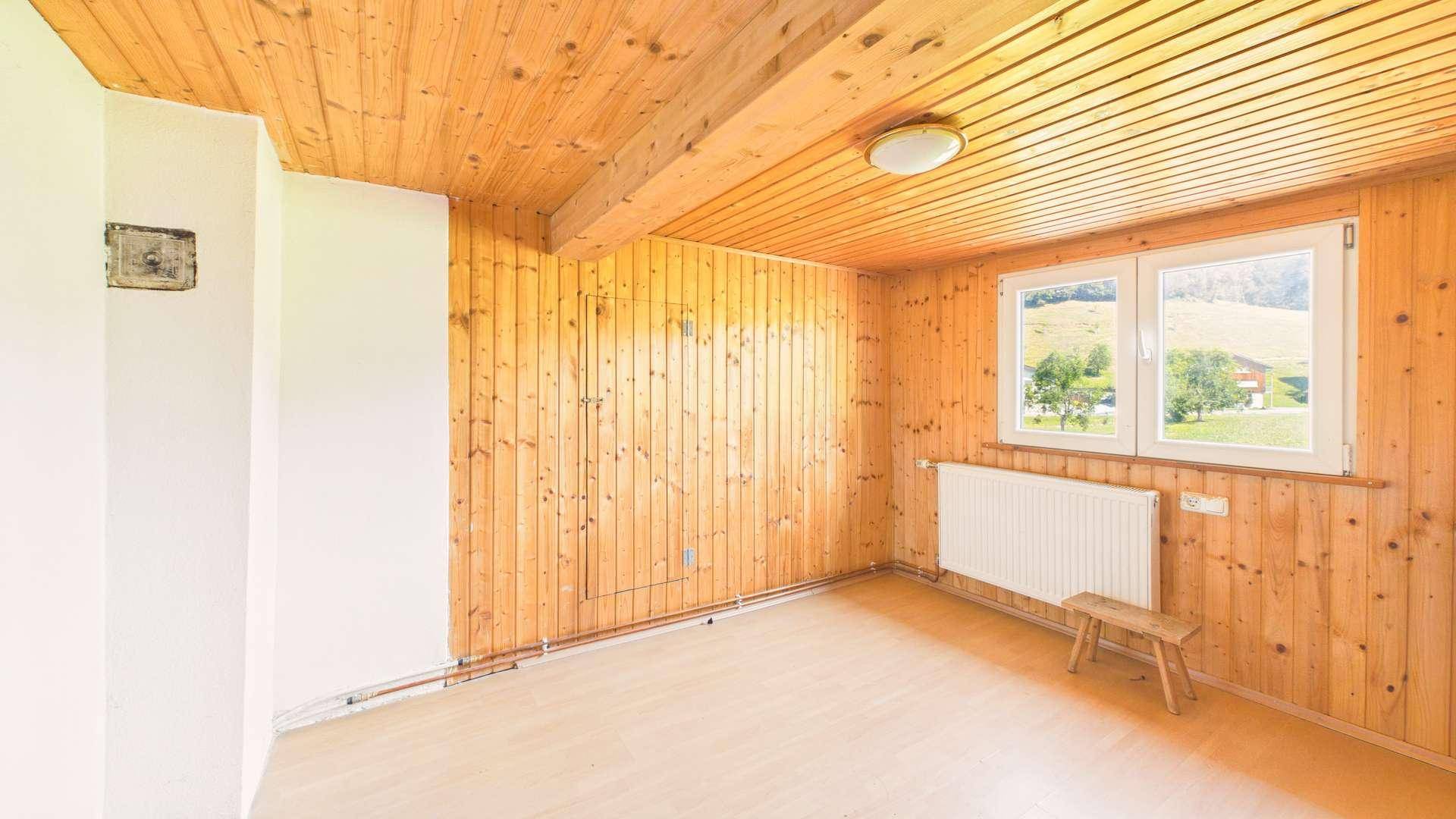 Heller Raum mit Holzverkleidung, weißer Wand und Fenster mit Blick ins Grüne.