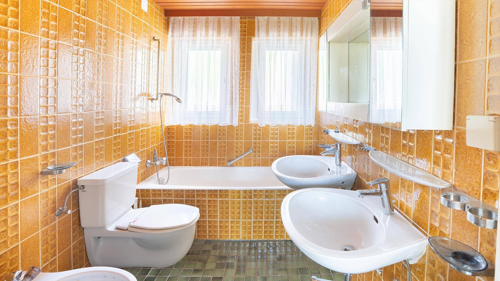 Badezimmer mit orangefarbenen Fliesen, zwei Waschbecken, Badewanne, WC und Bidet, mit Holzdecke.