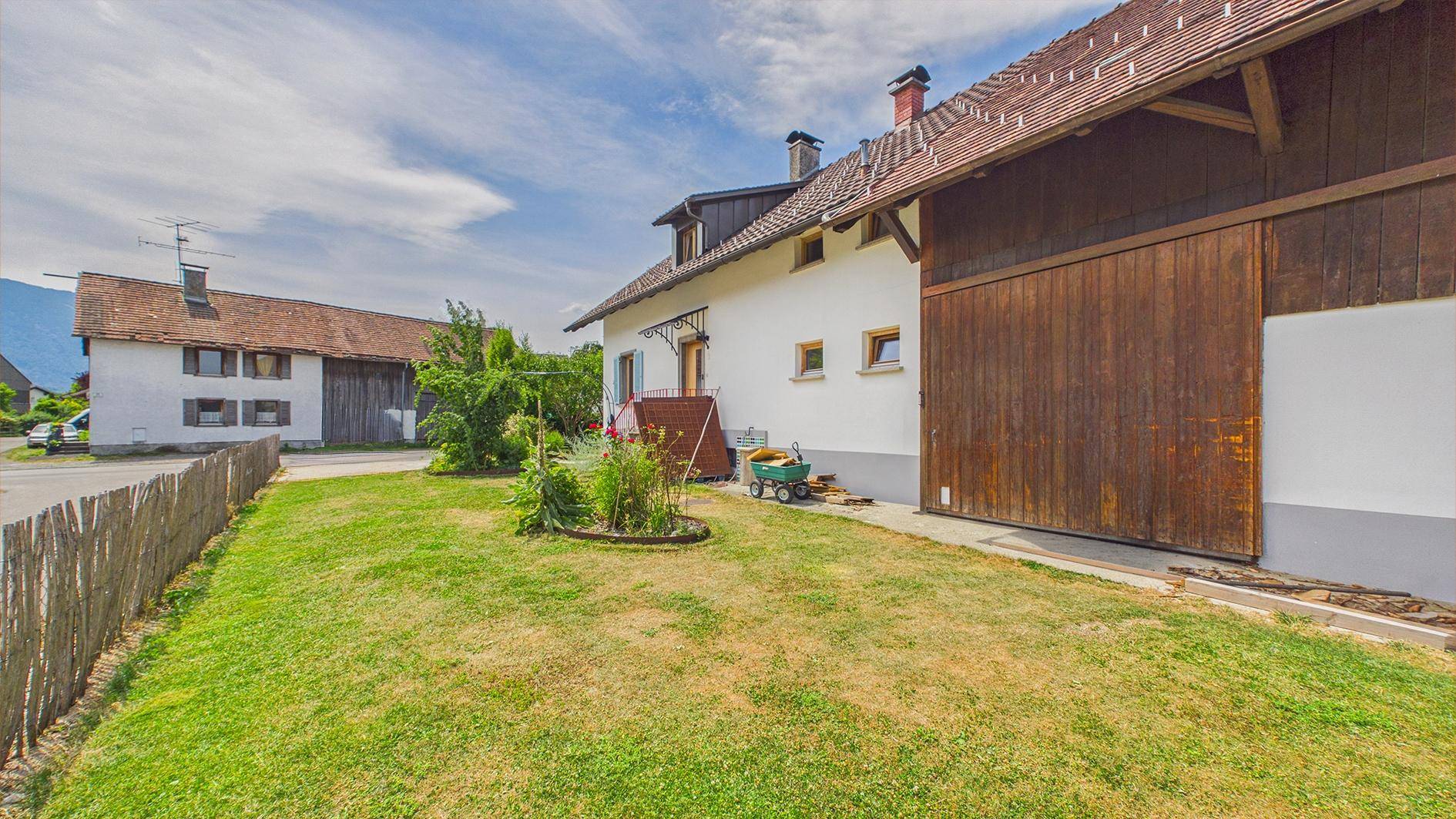 Seitenansicht des Hauses und der Scheune mit gepflegtem Rasen und Blumenbeet.