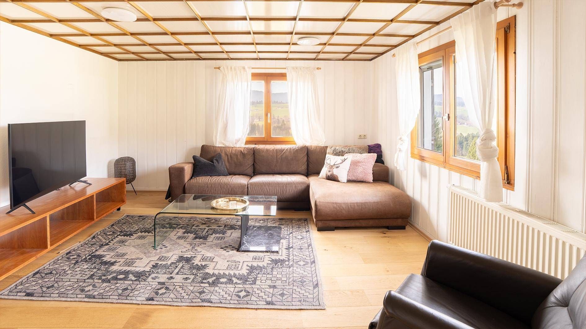 Helles Wohnzimmer mit Holzboden, bequemer Sofalandschaft und Blick ins Grüne.