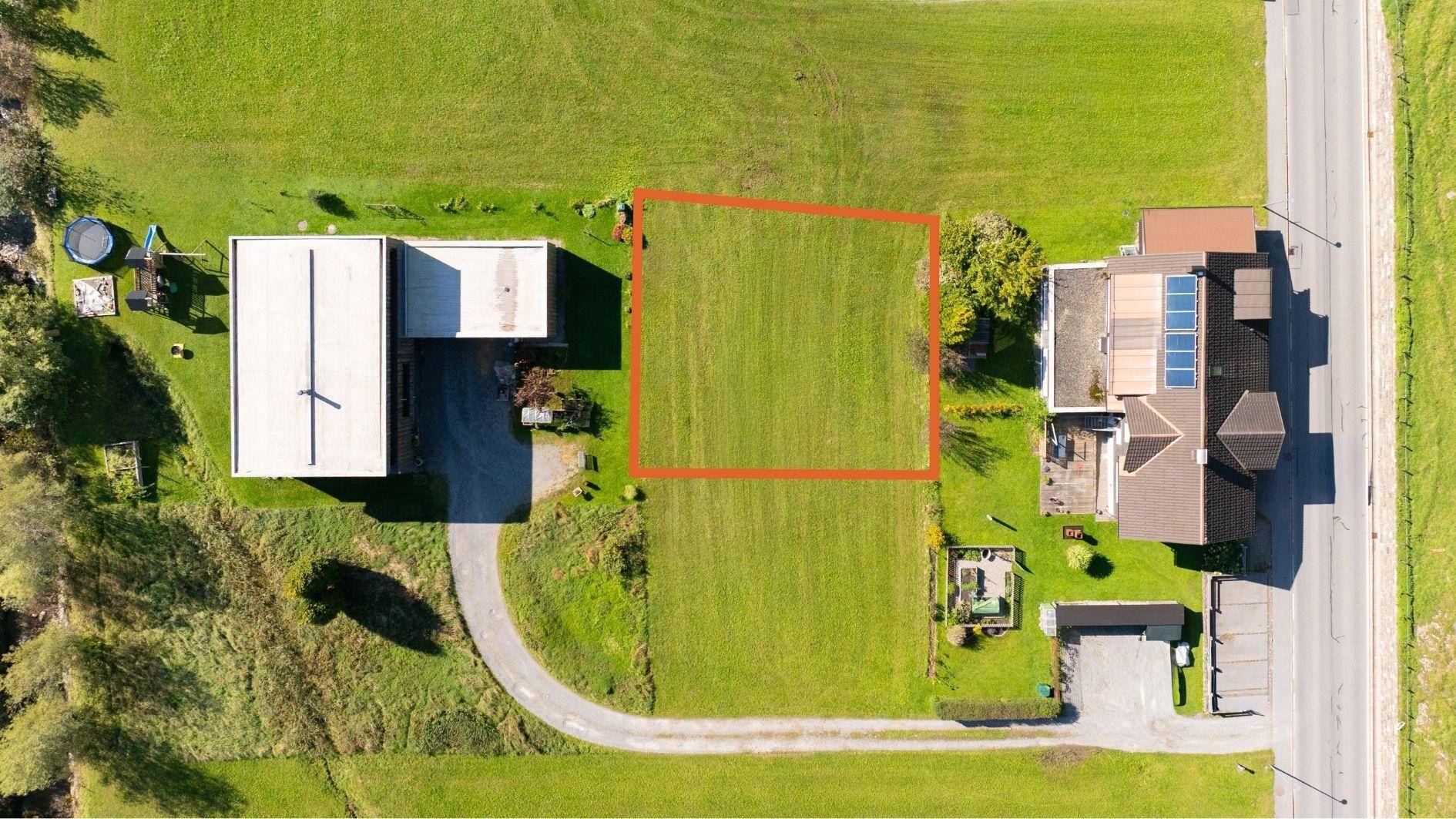 Übersichtliche Luftaufnahme eines Baugrundstücks, klar abgegrenzt durch eine rote Linie, in einer grünen Landschaft.