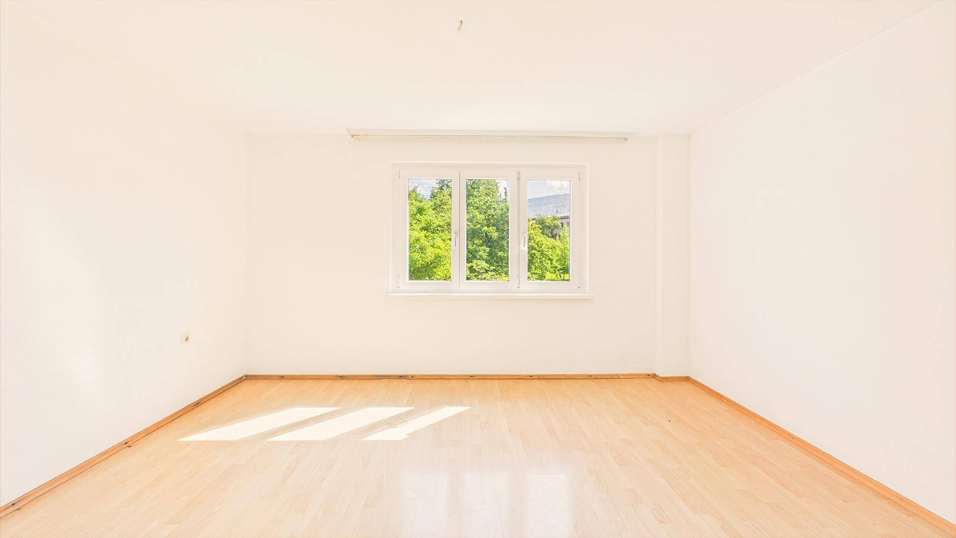 Leeres, helles Zimmer mit Parkettboden und großem Fenster, ideal als Schlafzimmer.