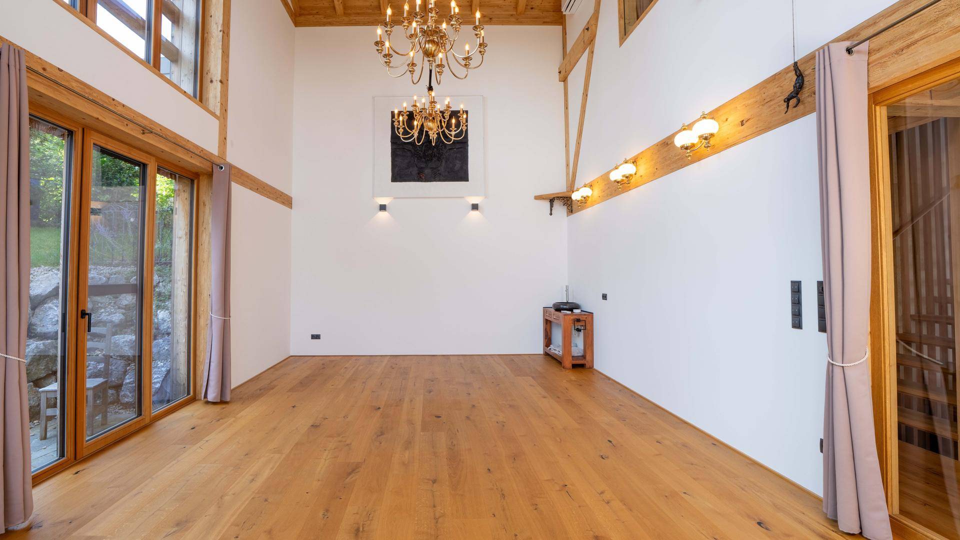 Geräumiger Wohnraum mit Holzboden, Kronleuchter und Zugang zu den großen Fenstern.