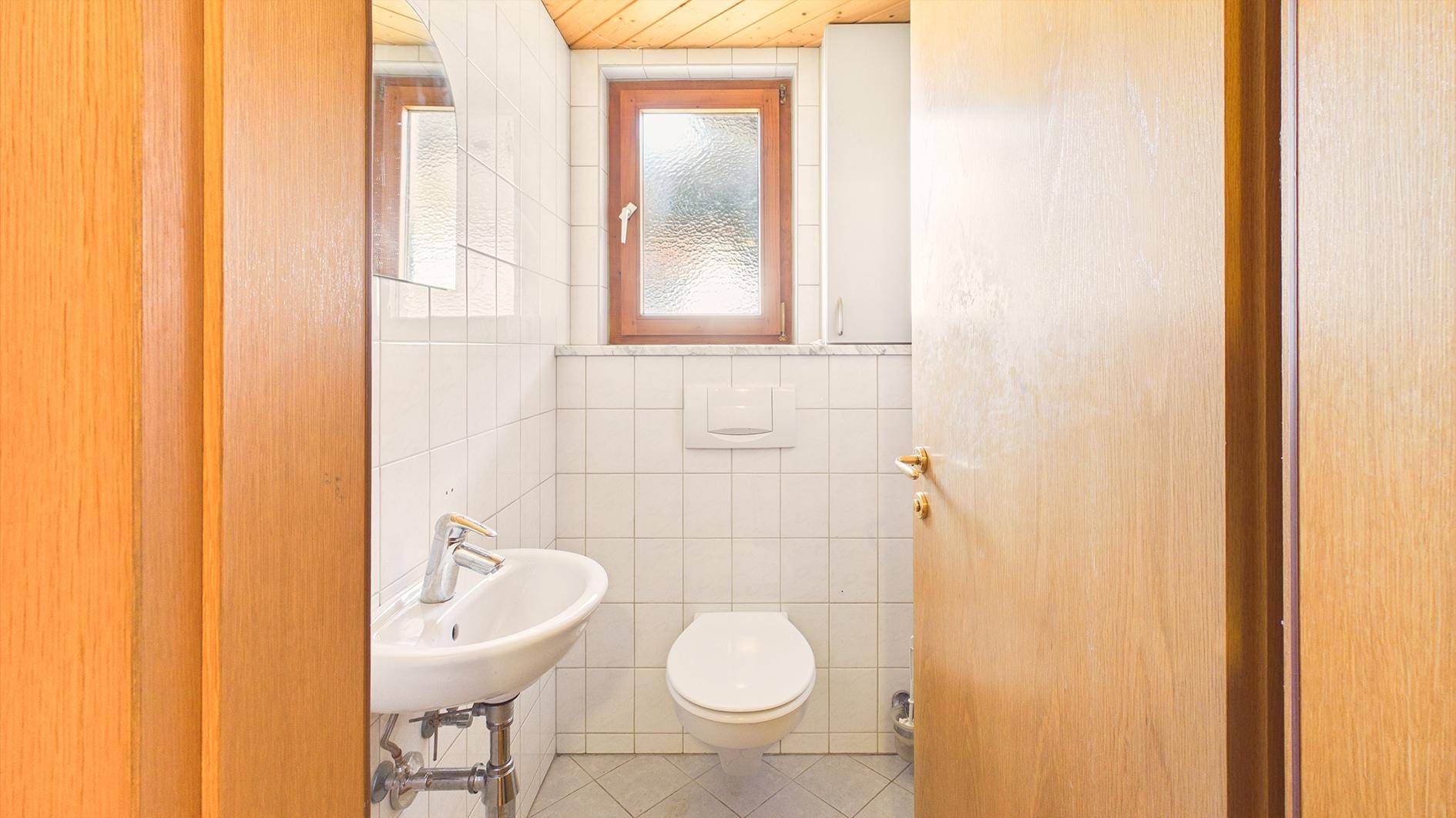 Kleines Gäste-WC mit weißen Fliesen, Waschbecken und Fenster für natürliche Belüftung.