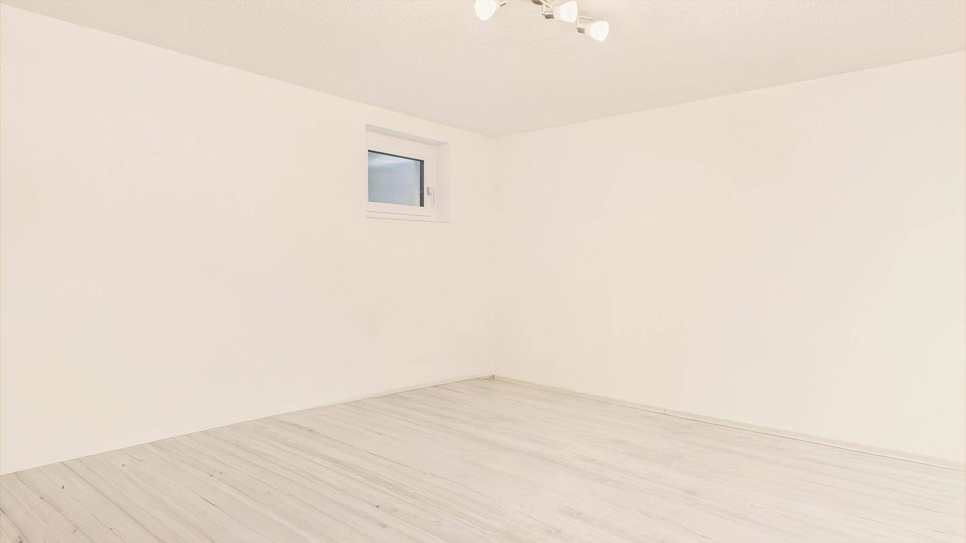 Leerer Raum mit hellem Holzboden und einem kleinen Fenster, vielseitig nutzbar.