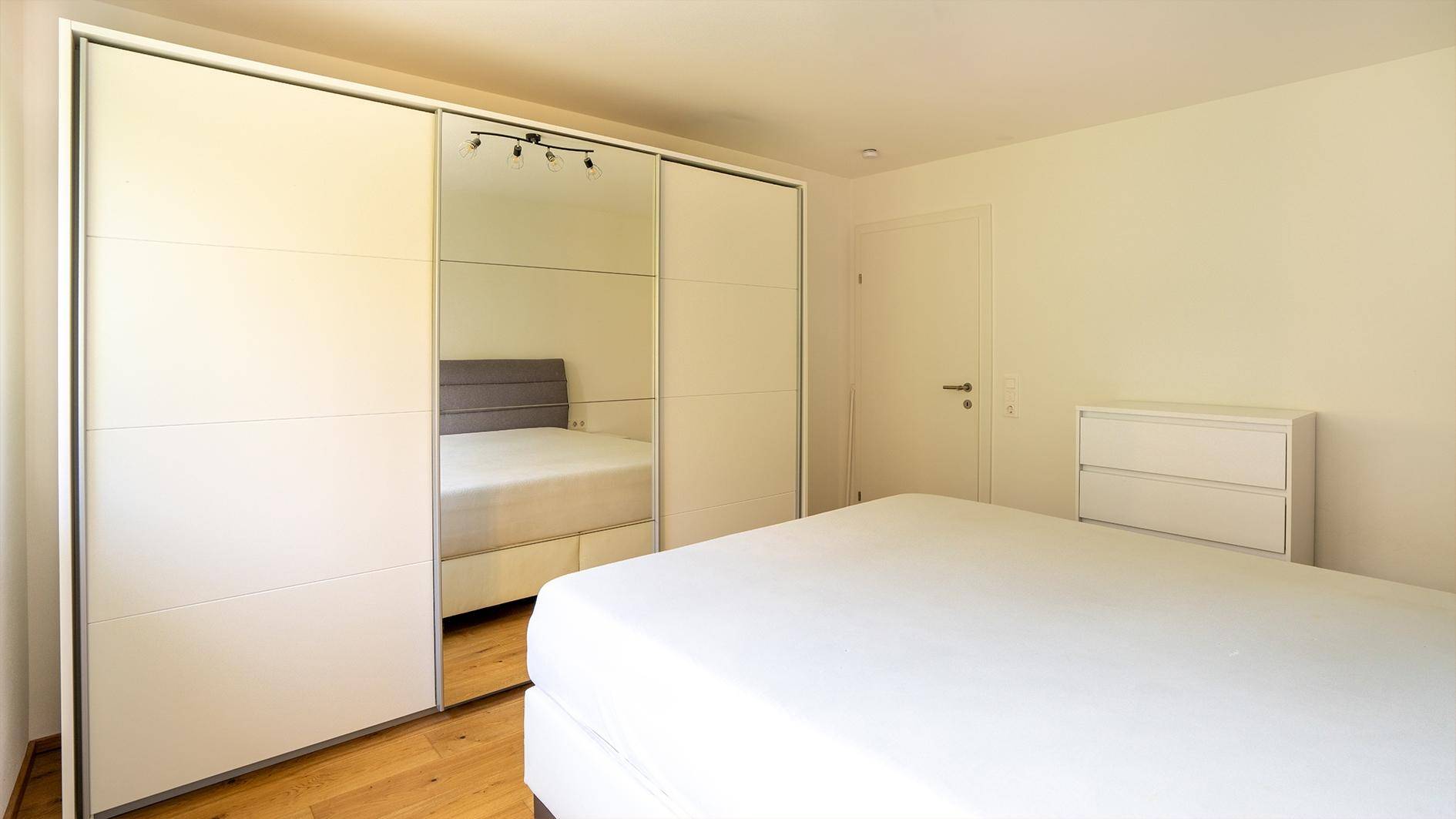Helles Schlafzimmer mit Doppelbett, großem Spiegelschrank und hellem Parkettboden.