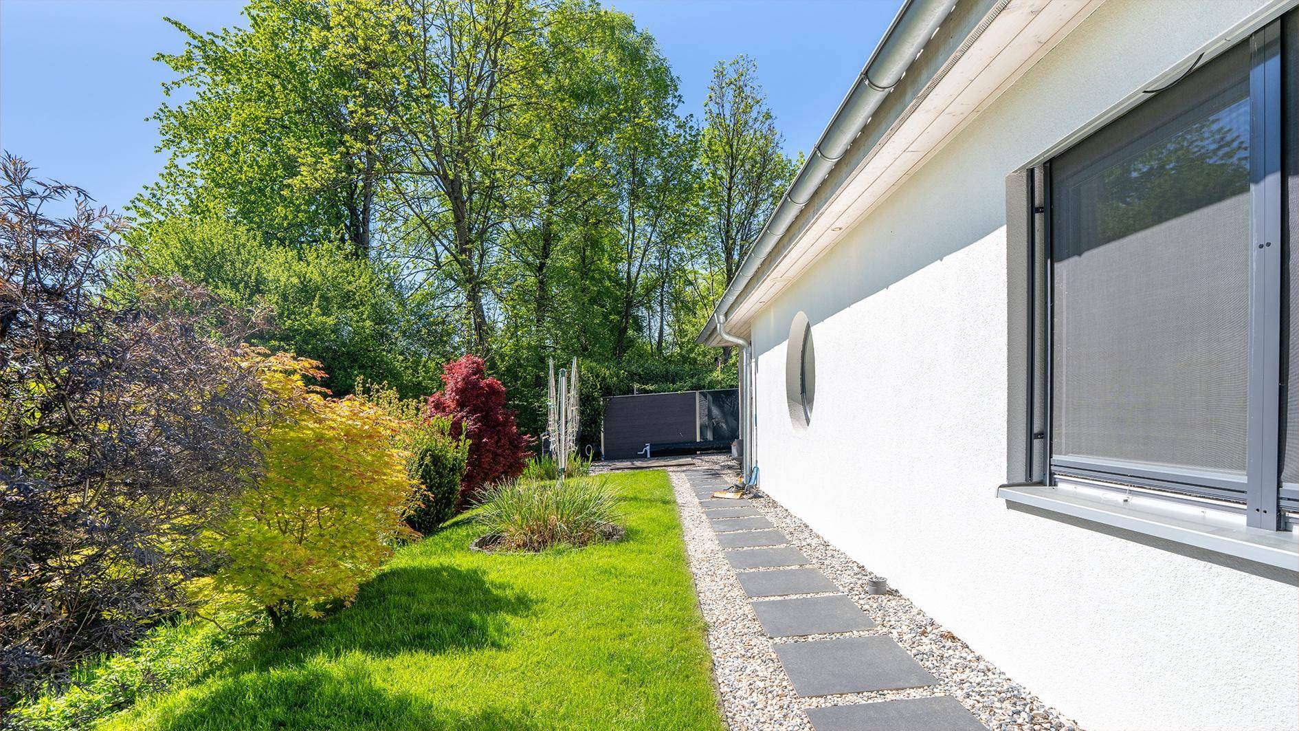 Gepflegter Gartenbereich neben dem Haus mit grüner Rasenfläche und einem Steinweg.