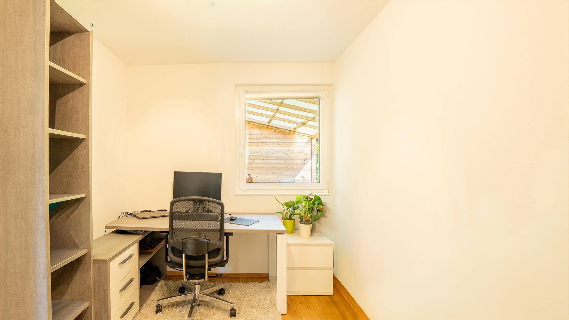 Helles Arbeitszimmer mit Schreibtisch, Bürostuhl, Computer und Bücherregal.