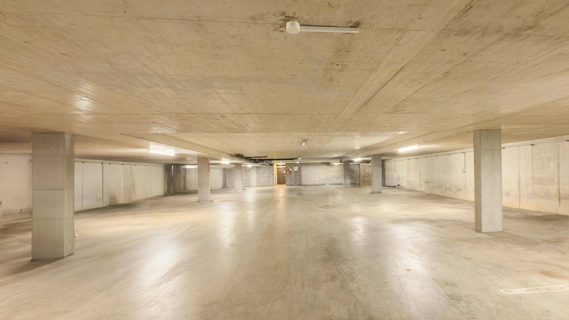 Geräumige Tiefgarage mit Betonboden und -decken, beleuchtet mit Reihen von Leuchtstofflampen.