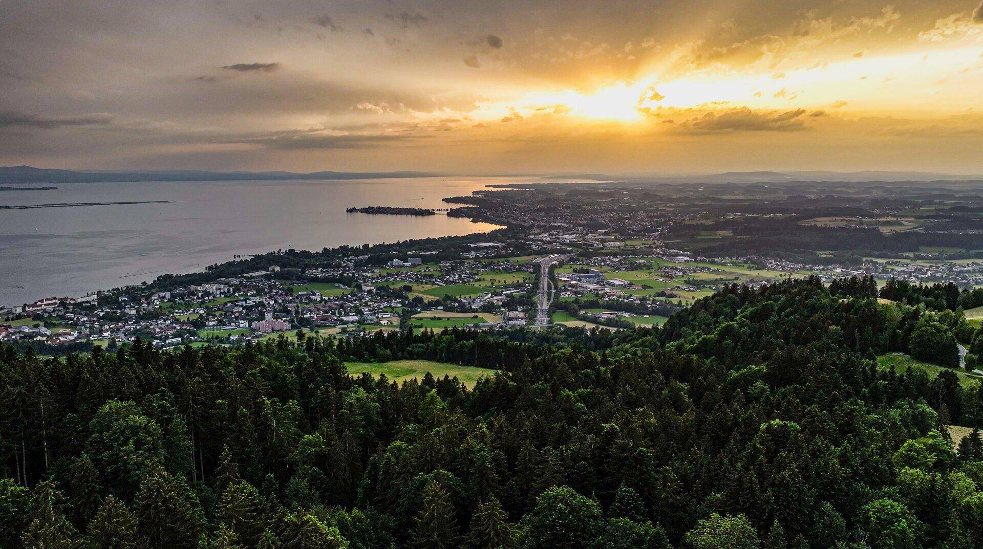Panoramablick auf den See, die Stadt und die umliegende Waldlandschaft bei Sonnenuntergang.