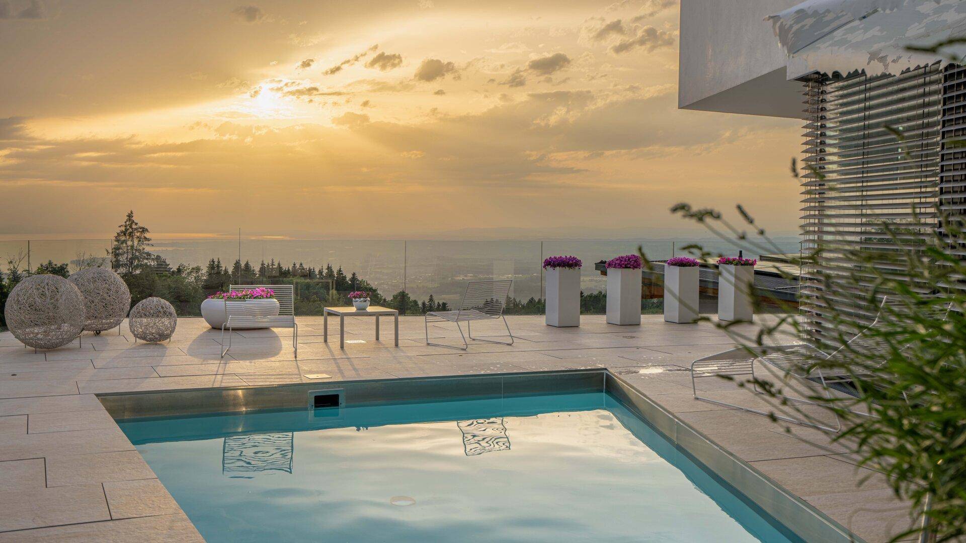 Großer Außenpool auf der Terrasse mit Liegebereich und spektakulärem Sonnenuntergang über der Landschaft.