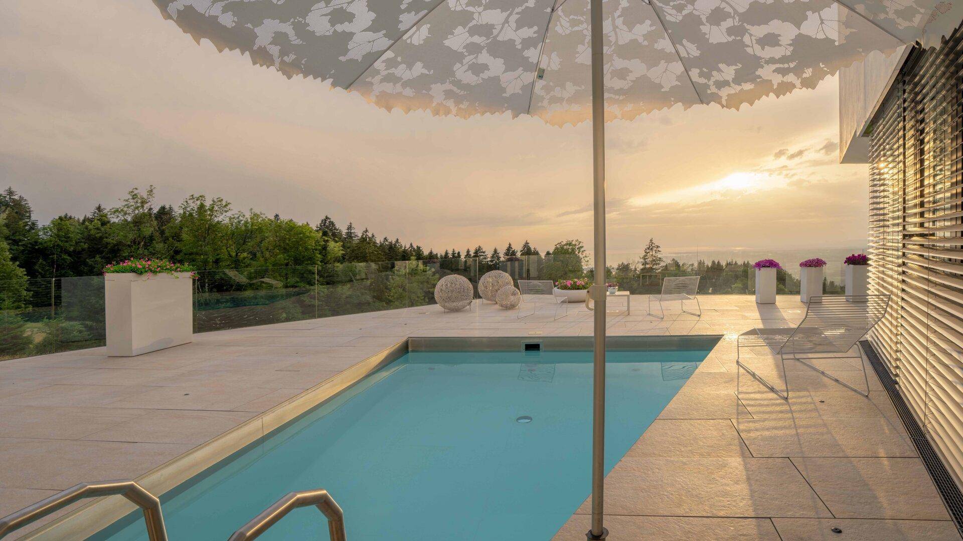 Großer Außenpool auf der Terrasse mit Liegebereich und spektakulärem Sonnenuntergang über der Landschaft.