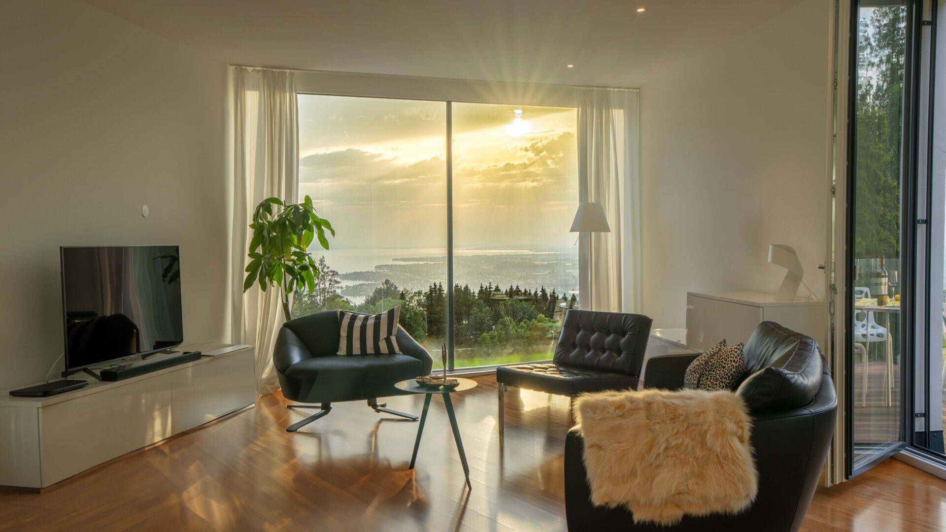 Lichtdurchflutetes Wohnzimmer mit Holzboden, bequemen Sesseln und atemberaubendem Ausblick auf die Landschaft.