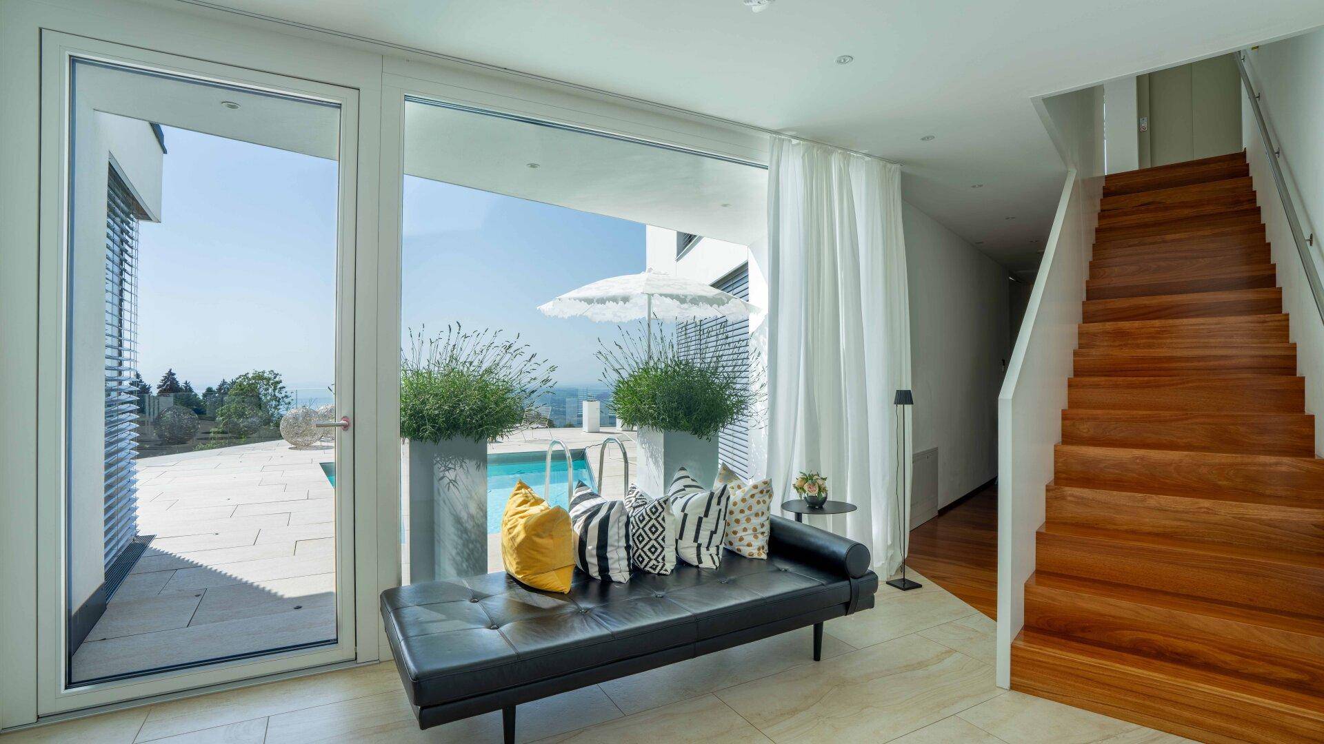 Heller Flur mit Holztreppe und Zugang zum Außenbereich mit Pool und Panoramablick.