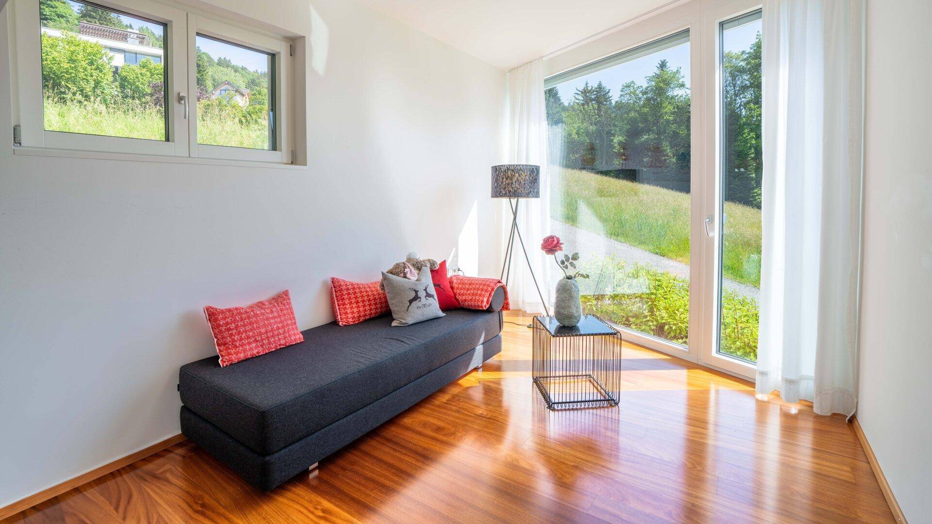 Gemütlicher Raum mit Tagesbett, Holzboden und großen Fenstern, die viel natürliches Licht hereinlassen.