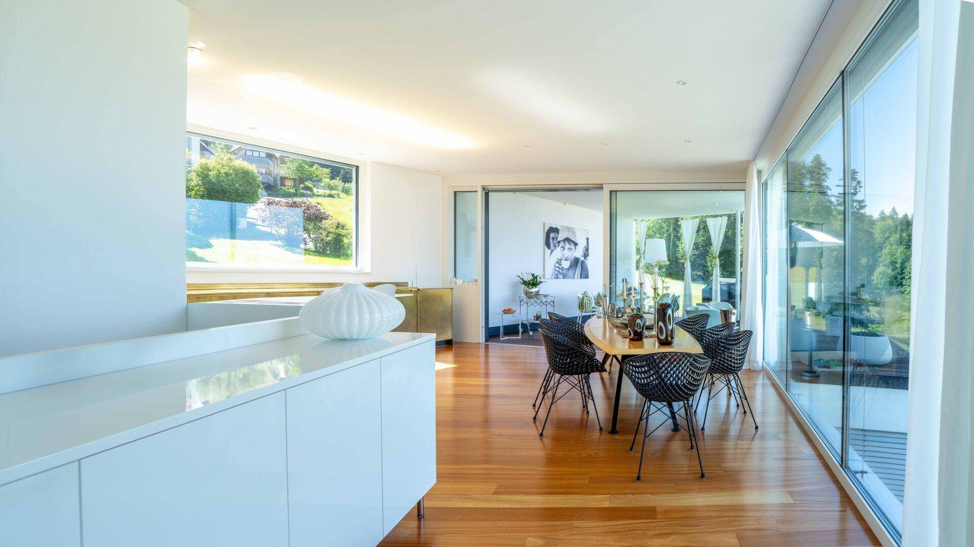 Heller Essbereich mit Holzboden, modernen Möbeln und großen Fensterfronten mit Blick ins Grüne.