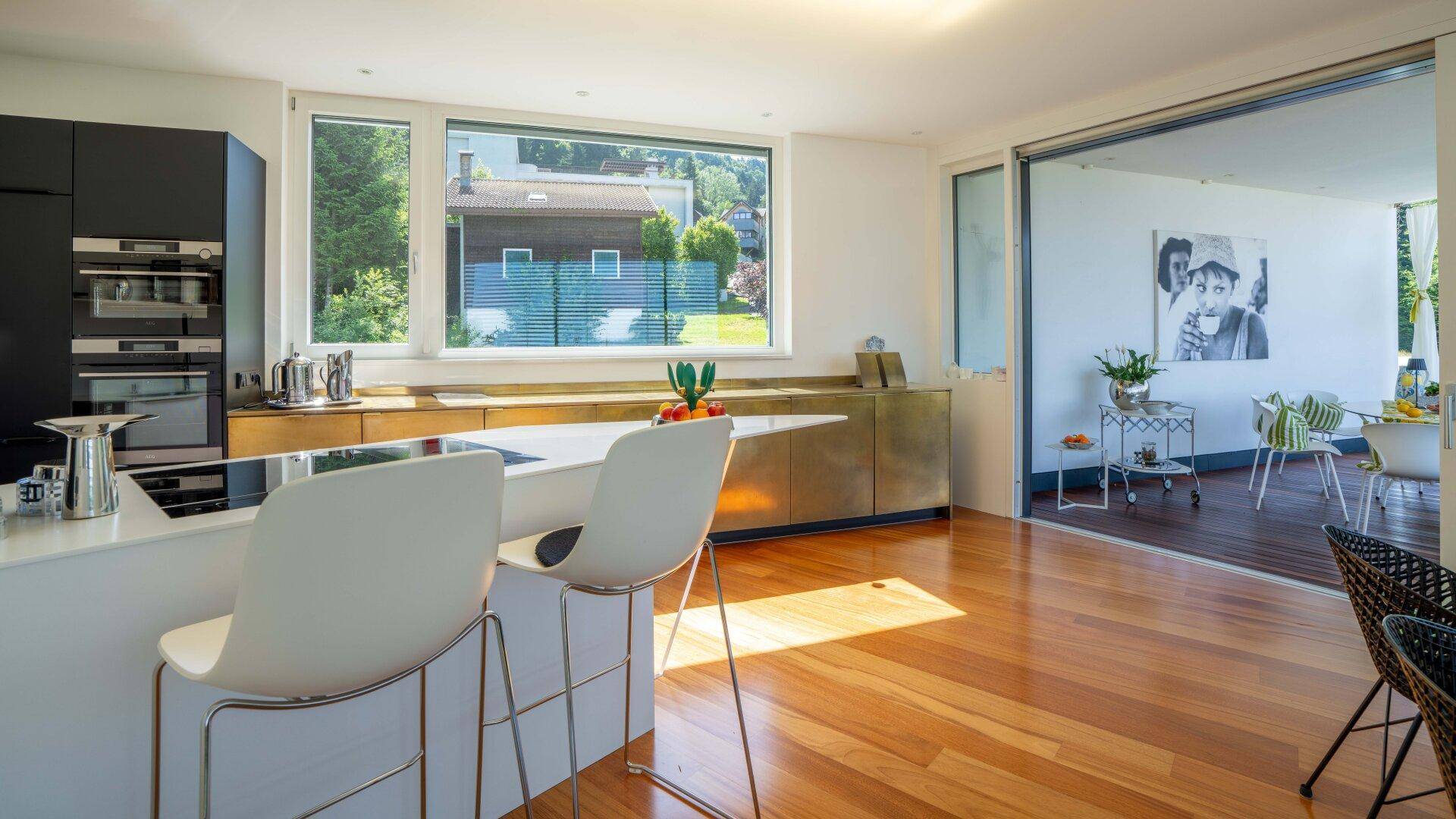 Helle Küche mit goldenen Fronten, Frühstücksbar und Zugang zu einem Außenbereich mit Sitzgelegenheiten.