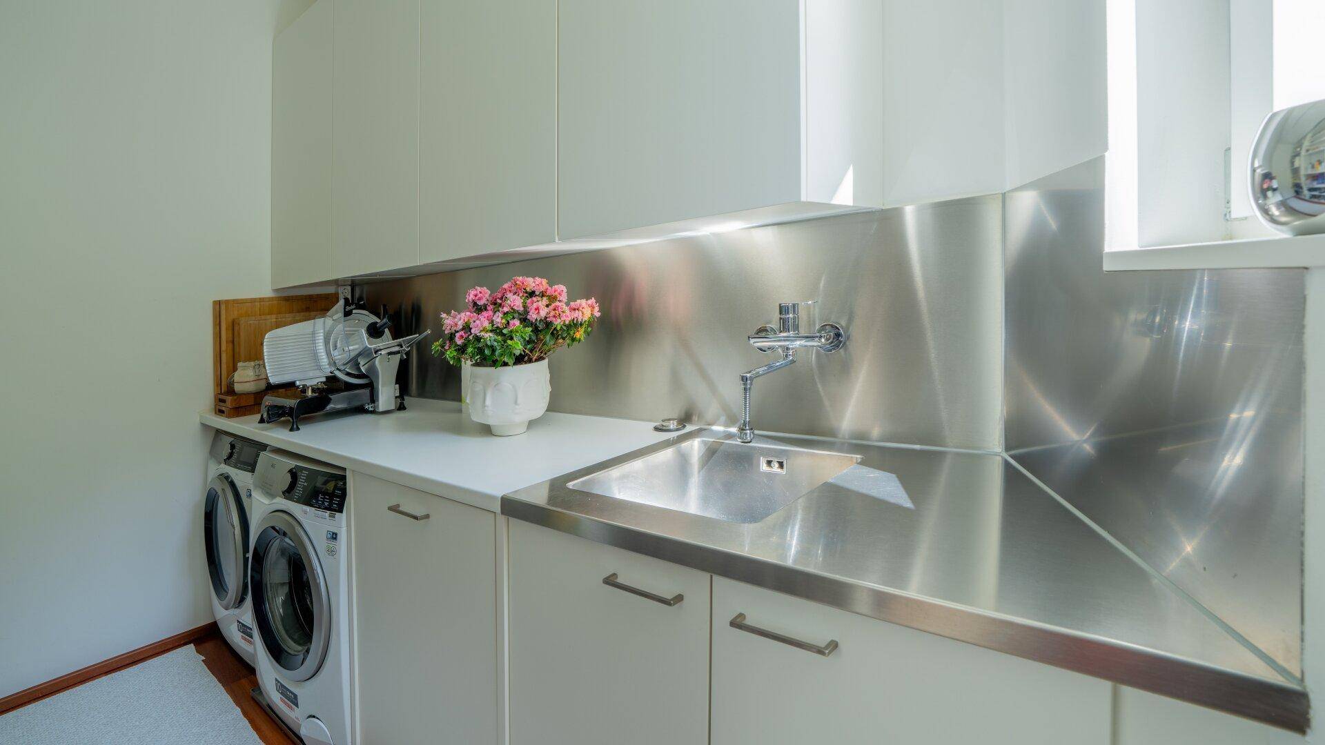 Funktionaler Hauswirtschaftsraum mit Waschmaschine, Trockner und Edelstahlspüle für den täglichen Gebrauch.
