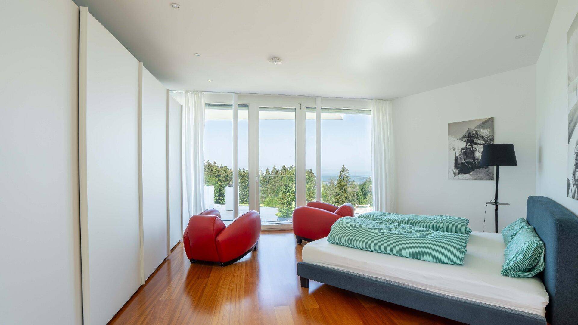 Helles Schlafzimmer mit Einbauschränken, Holzboden und großen Fenstern mit weitem Ausblick.