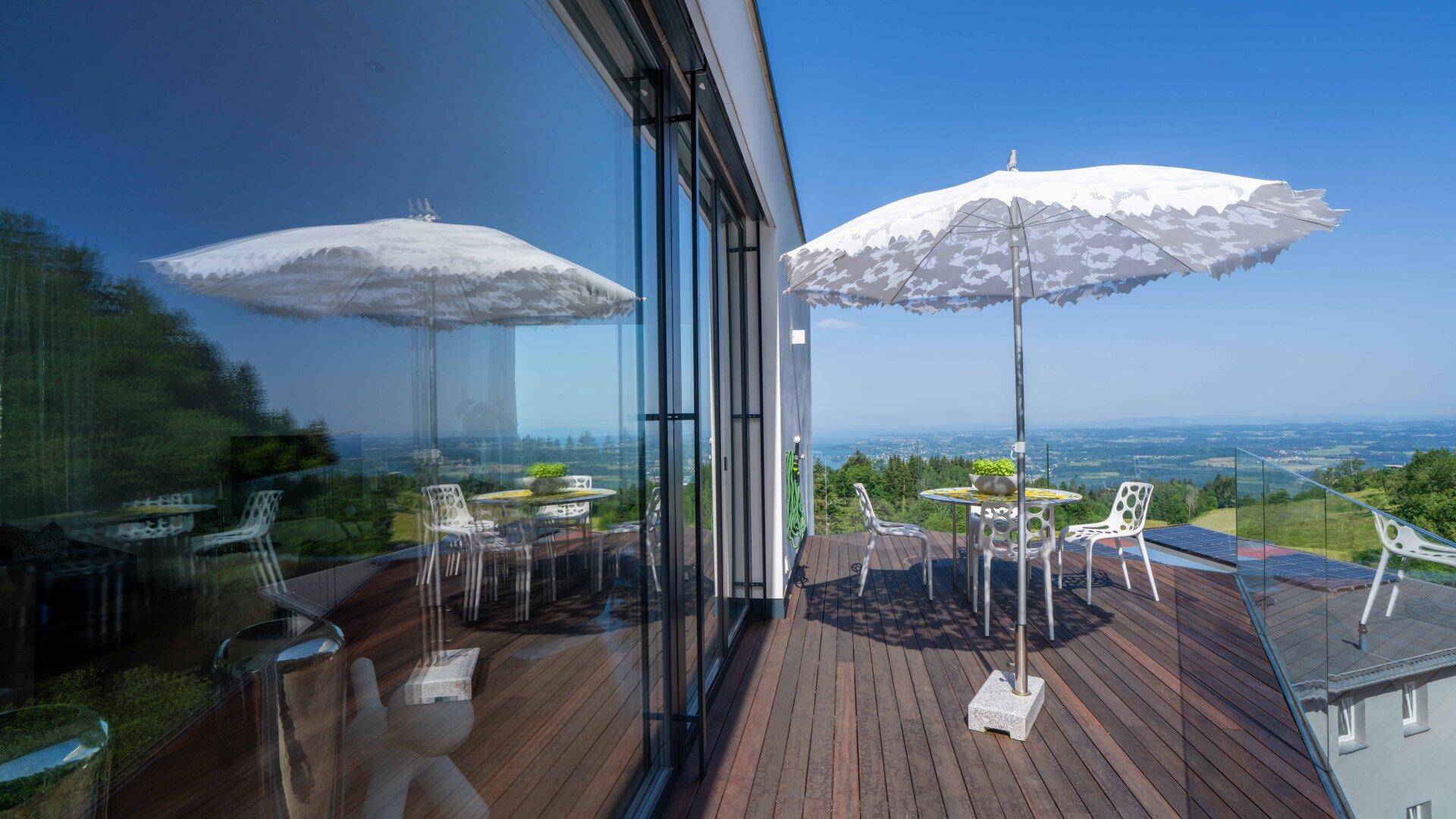 Sonnige Terrasse mit Esstisch, Sonnenschirm und atemberaubendem Weitblick über die Landschaft.