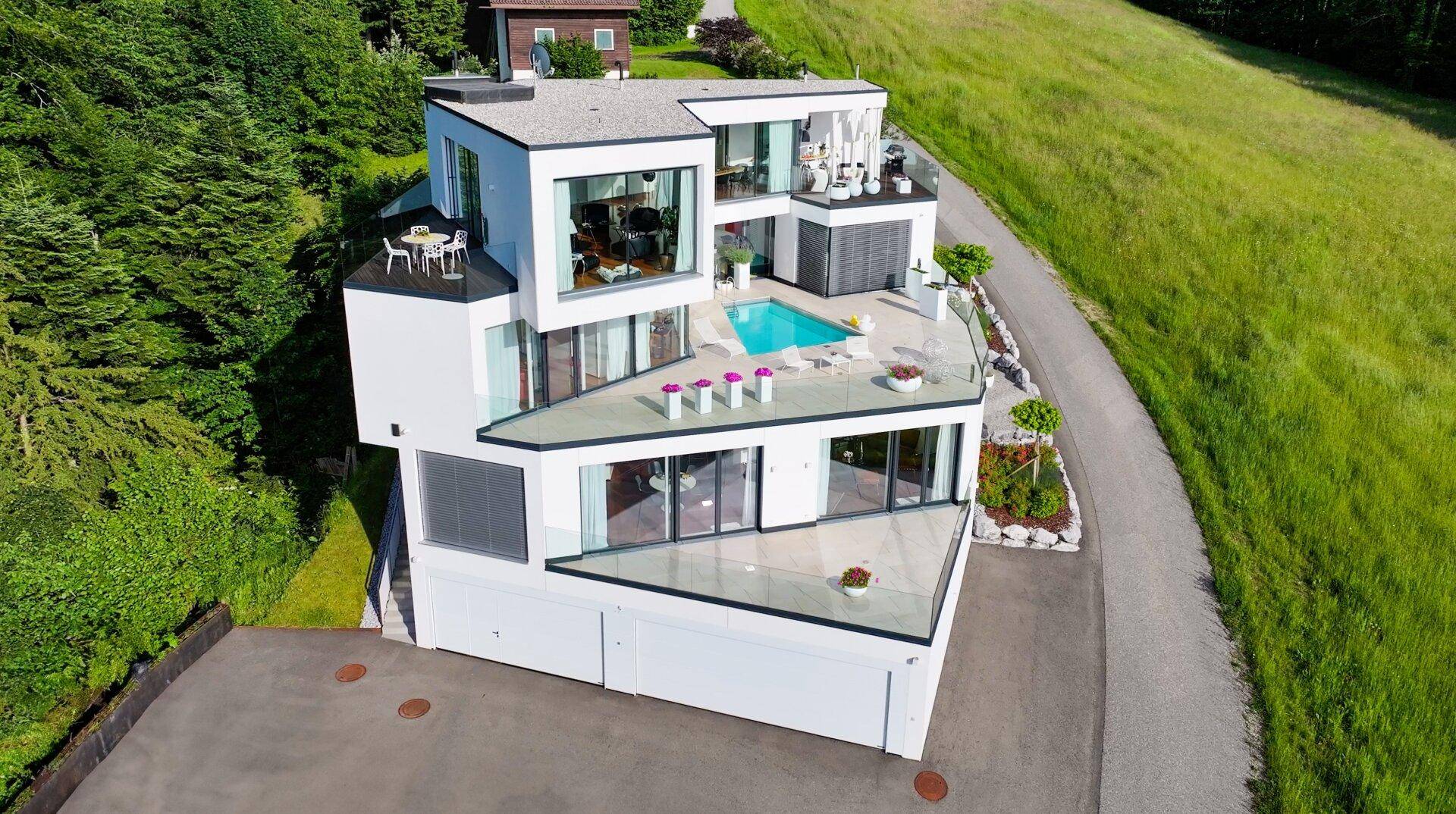 Luftaufnahme der modernen Villa mit Pool, Terrassen und der umliegenden grünen Landschaft.