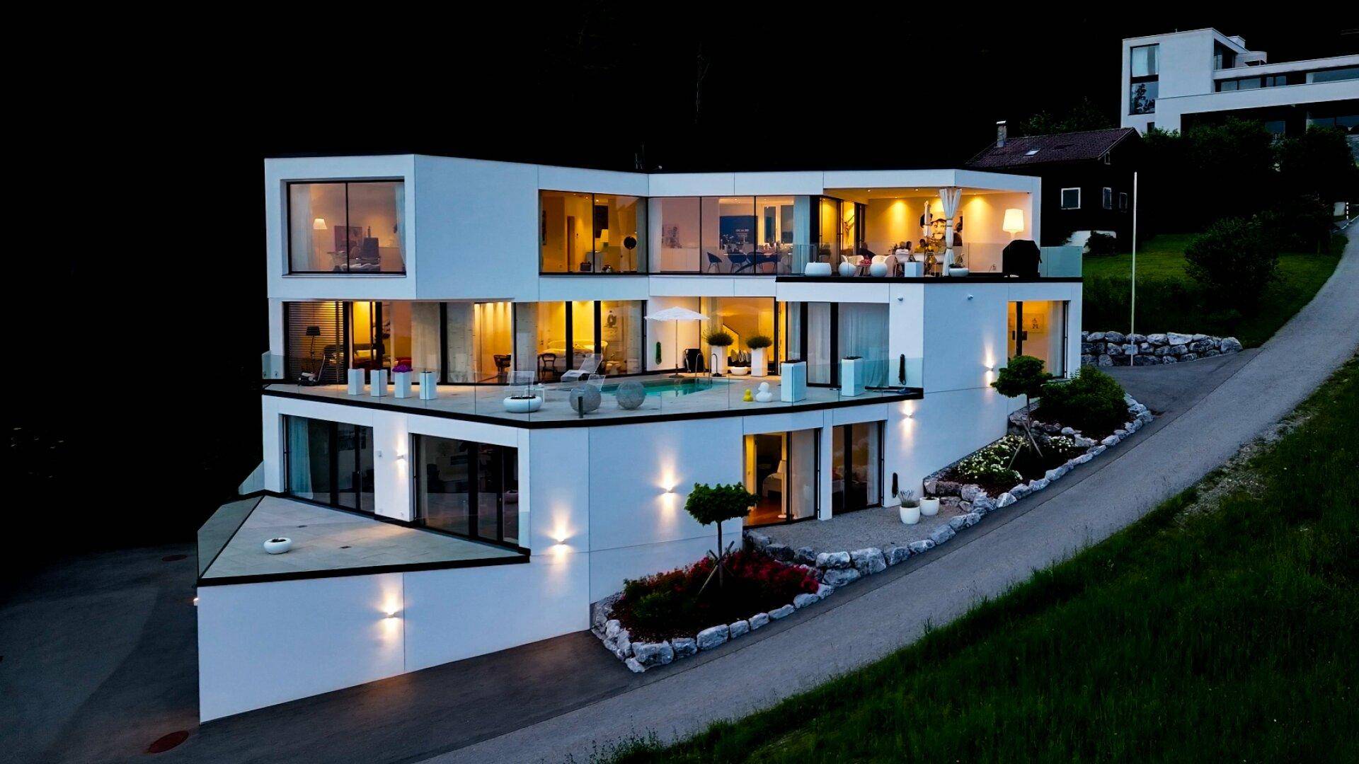Die moderne Villa bei Nacht, eindrucksvoll beleuchtet, mit großen Fensterfronten und Terrassen.