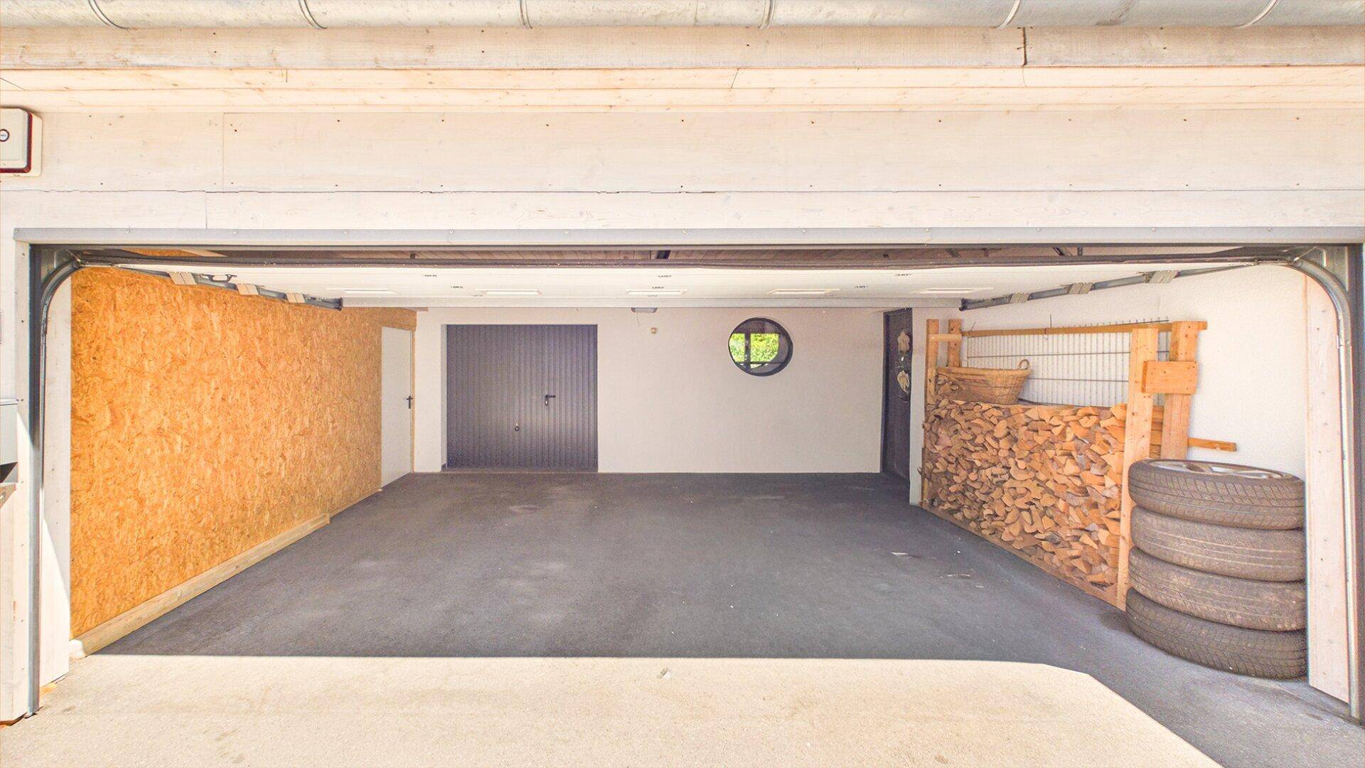 Große Garage mit viel Stauraum, Holzstapeln und einem runden Fenster.