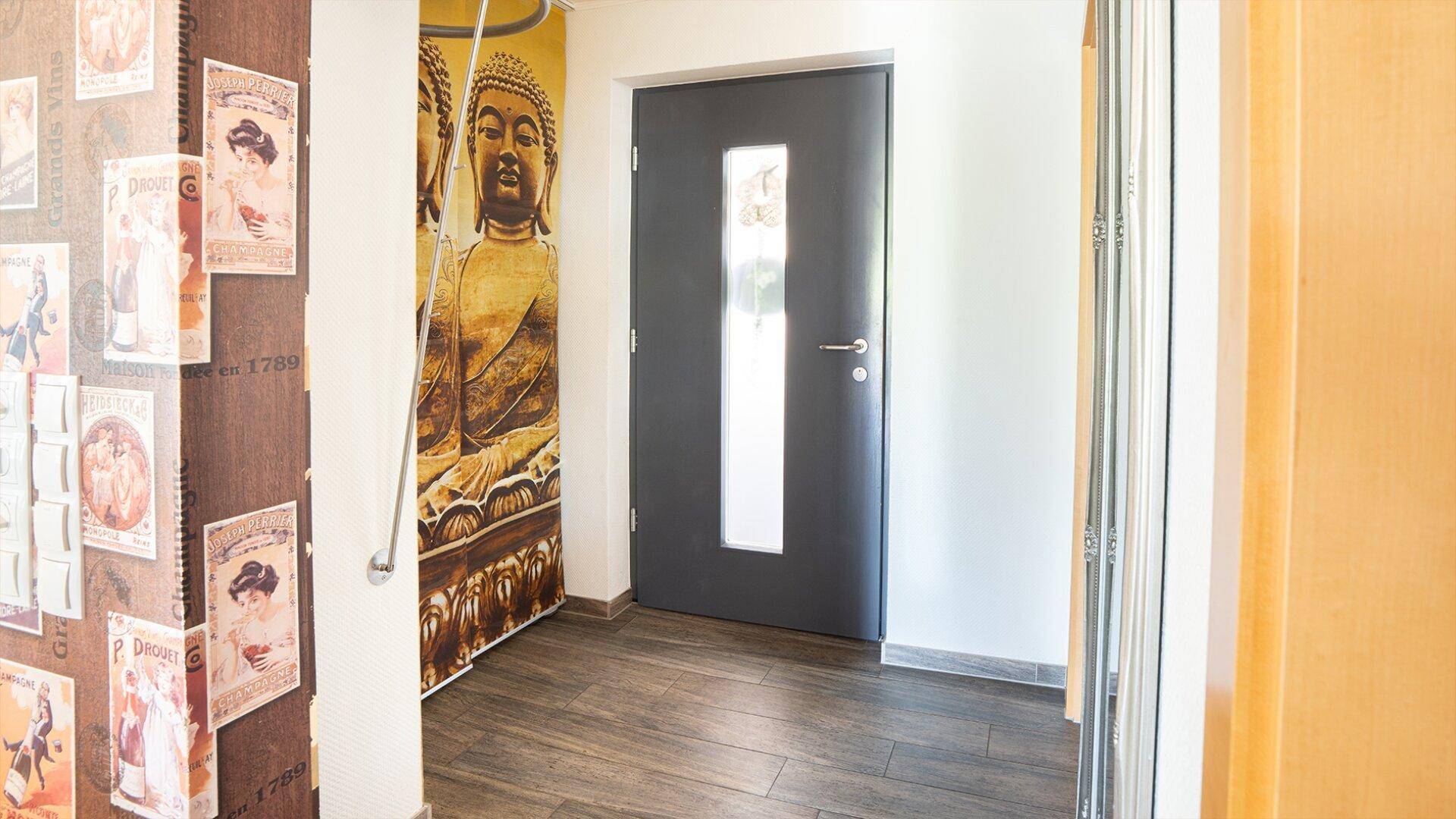 Eingangsbereich mit dekorativer Buddha-Wandmalerei und moderner Eingangstür.