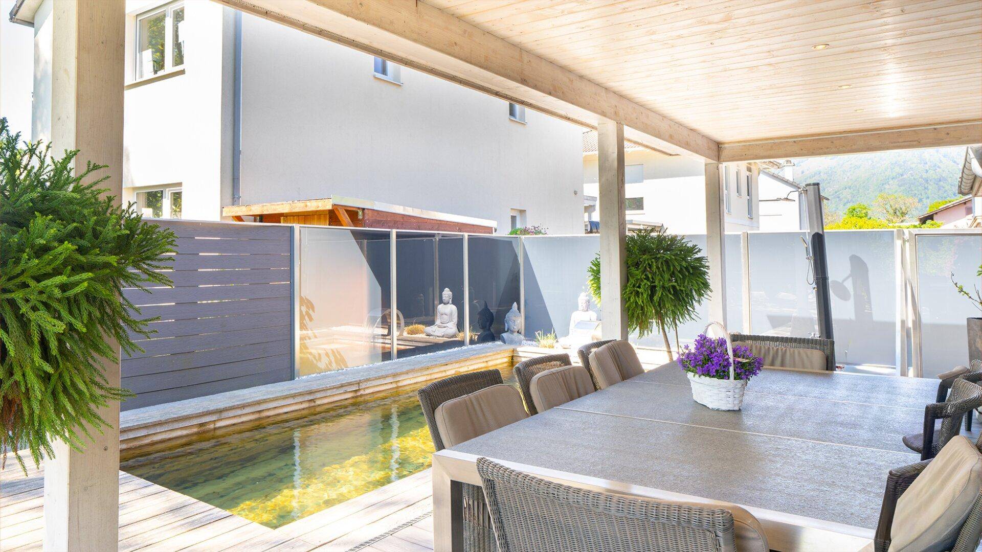 Überdachte Terrasse mit Essbereich und Blick auf das Wasserbecken und die Nachbarschaft.