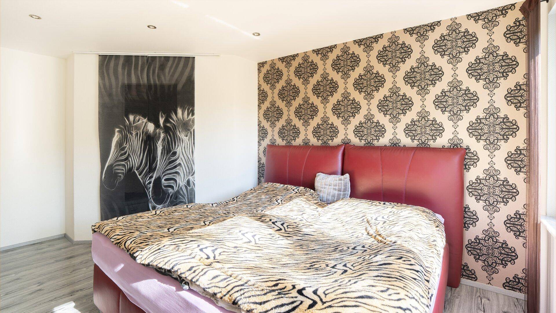 Helles Schlafzimmer mit gemusterter Tapete, großem Bett und dekorativem Zebra-Bild.