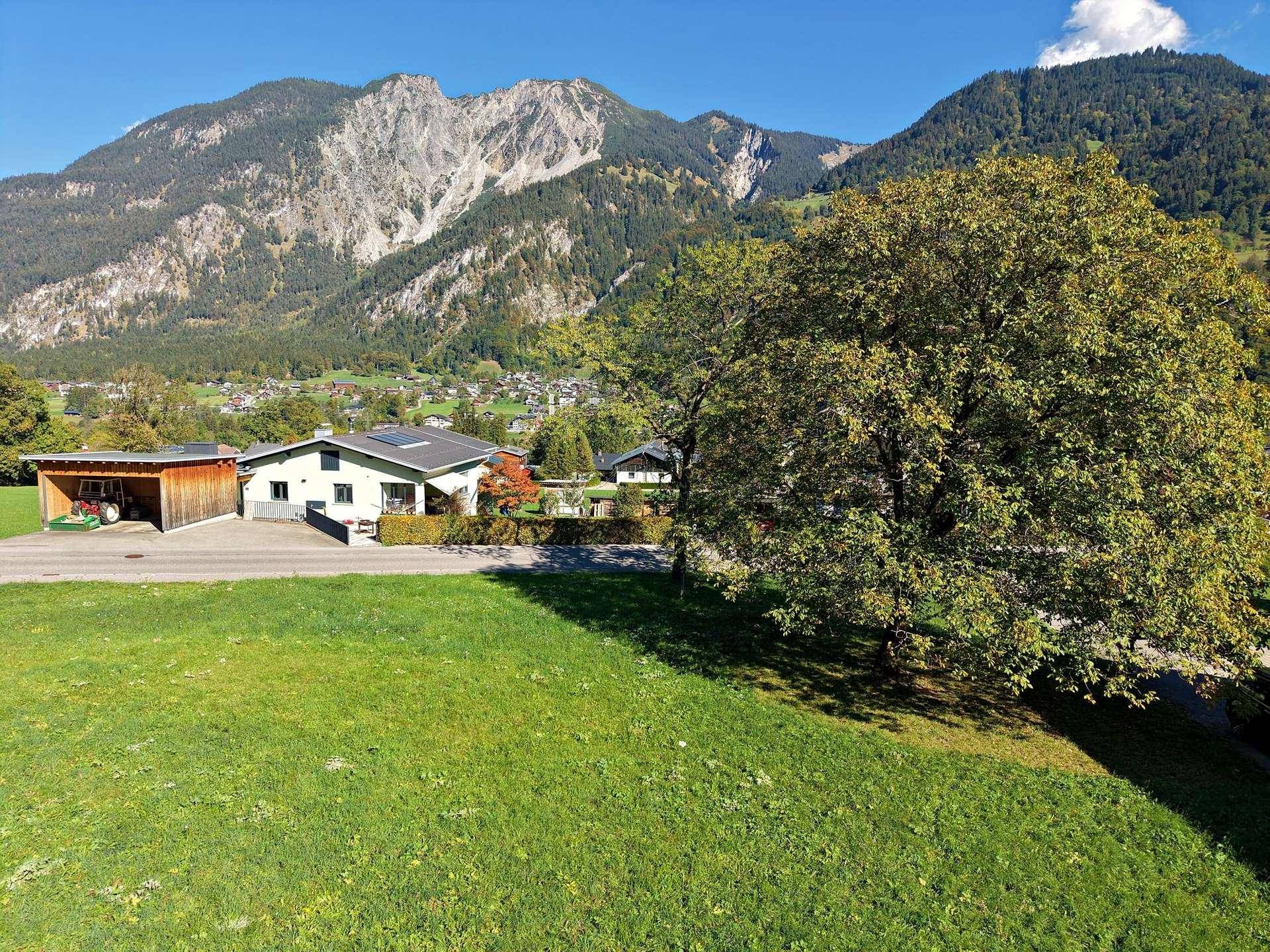Haus mit großem Baum im Vordergrund und majestätischer Berglandschaft im Hintergrund.